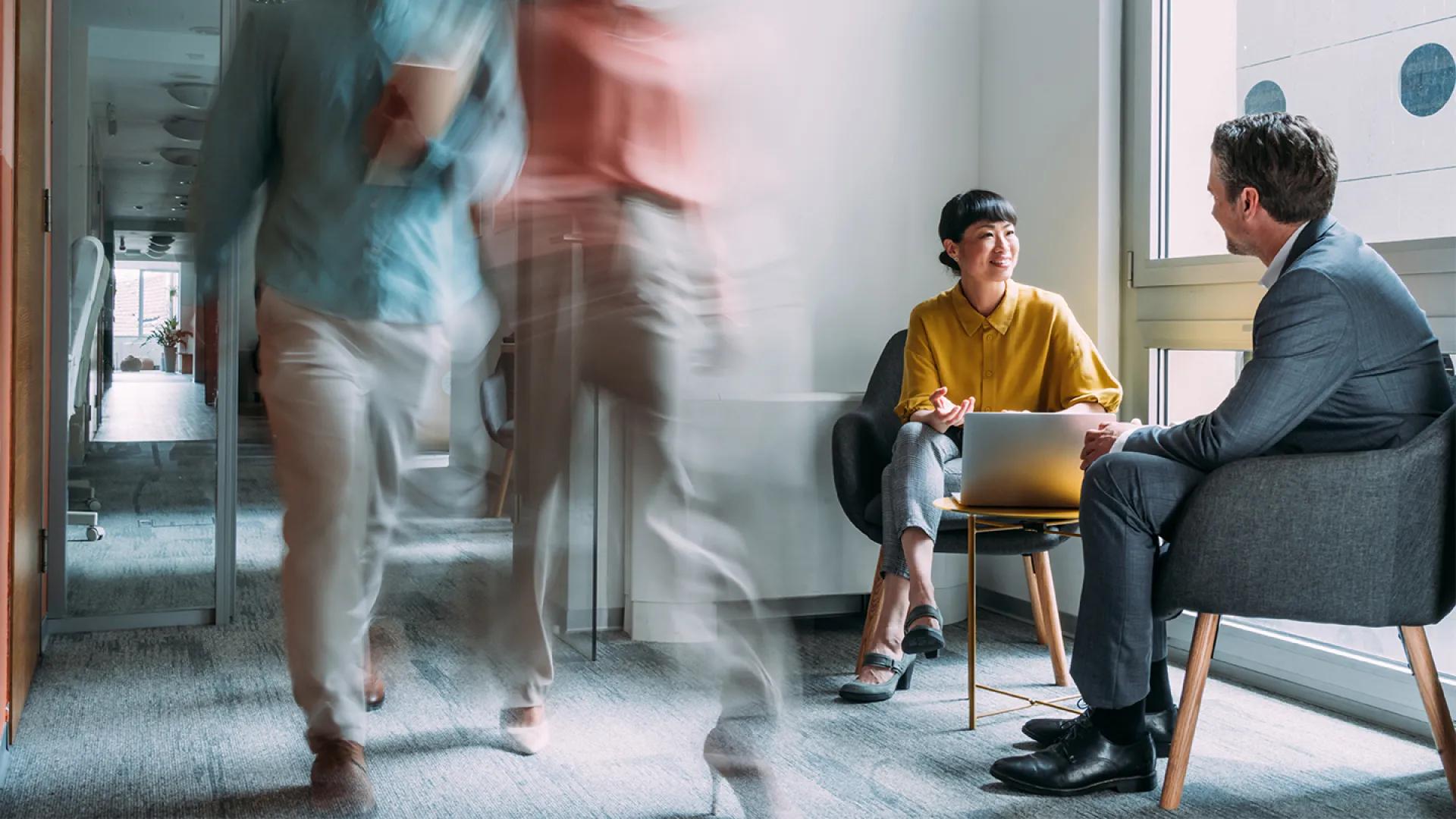 two business people talking in chairs in a busy hallway