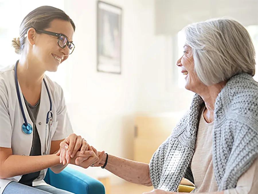 Doctor and elderly patient smile holding hands.