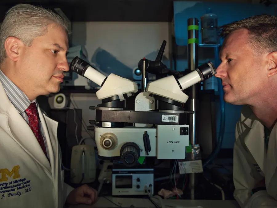 Two researchers look in microscopes facing one another