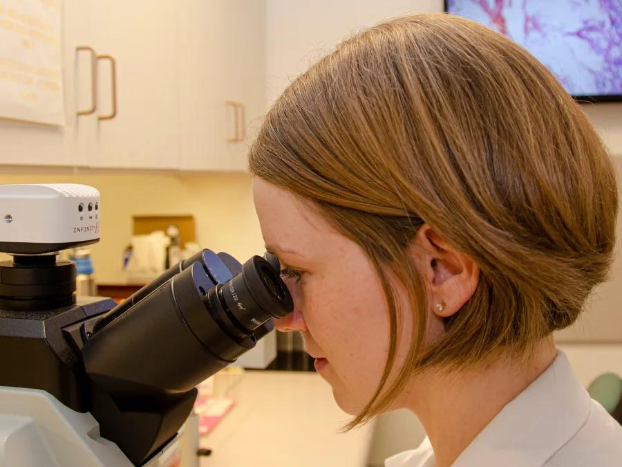 A woman in a lab coat looking through a microscope, conducting scientific research