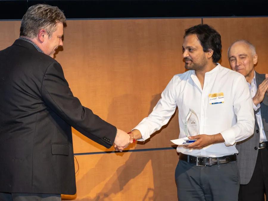 An award recipient accepts a trophy from a presenter at the MIP PostDoc event