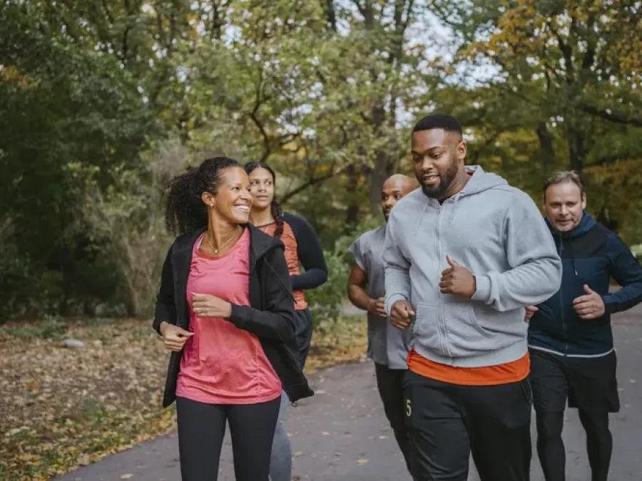 group of multicultural men and women running and smiling on a wooded path