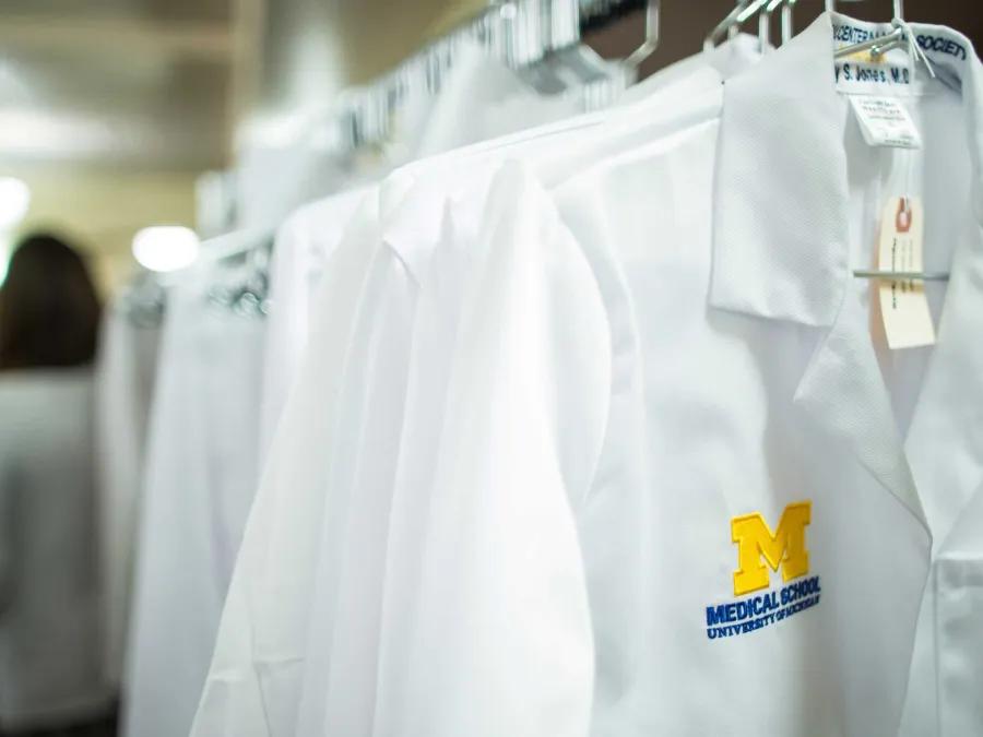 Coat rack with white coats embroidered with Michigan Medicine logo