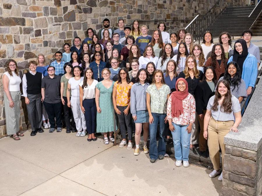 large group of graduate students standing together in front of a brick wall