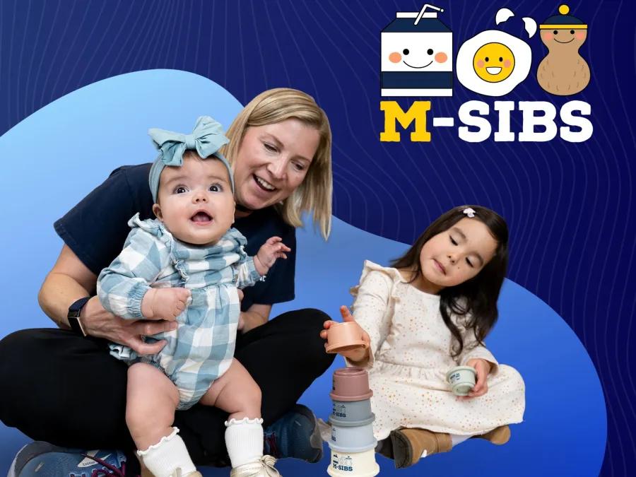 A University of Michigan nurse plays with an infant in a blue-checked headband while a four-year-old girl plays beside her with a stacking toy