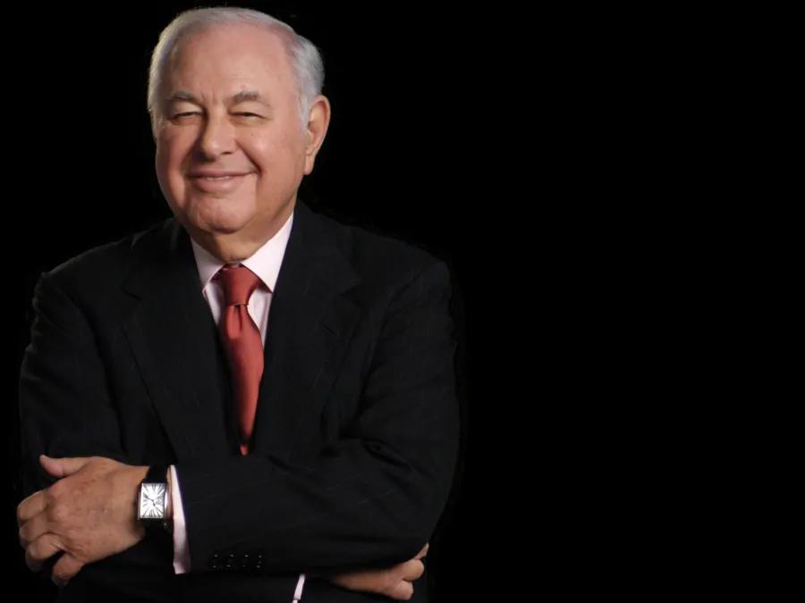 A. Alfred Taubman, smiling, in a dramatic portrait wearing dark suit against a dark background