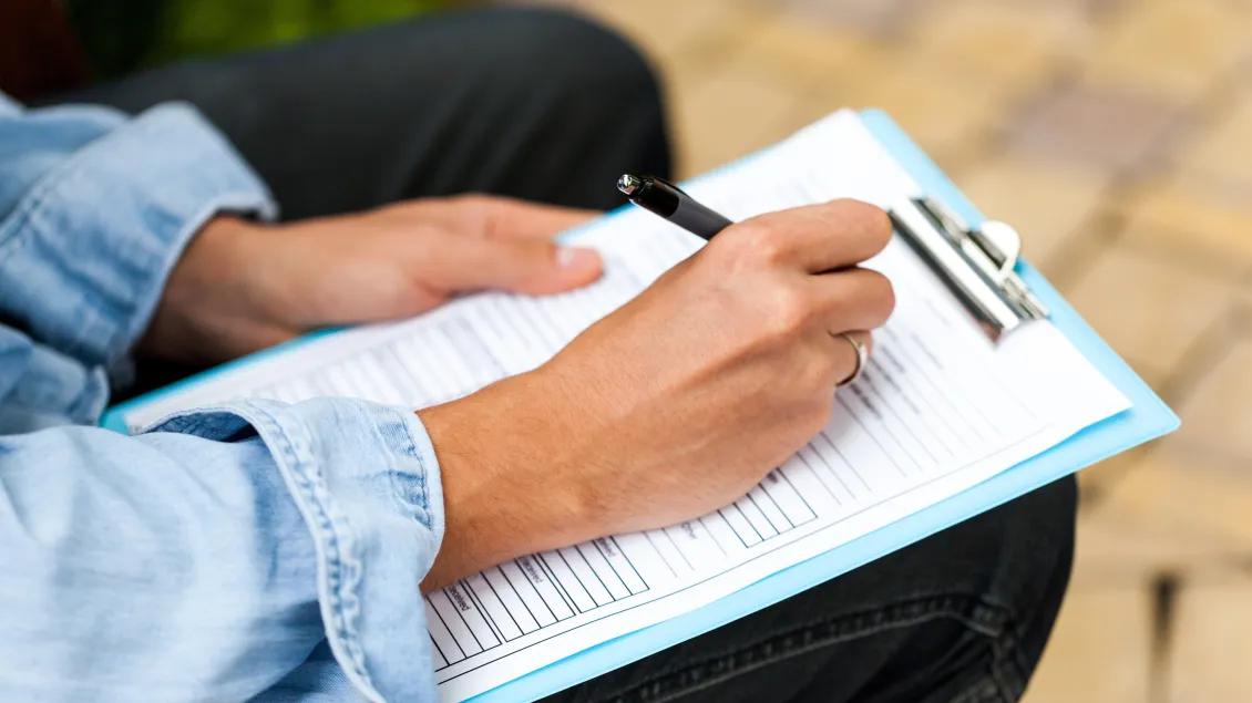 close-up of hands filling out form on clipboard