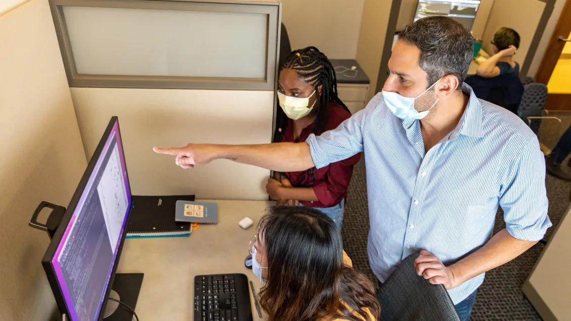 Professor Evan Snitkin points at computer screen while mentoring students.