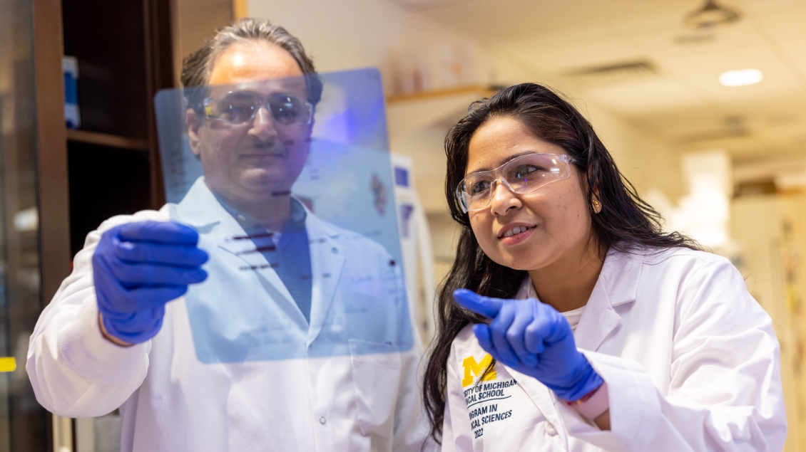 Professor Ajit looks through a clear sheet while standing next to a trainee