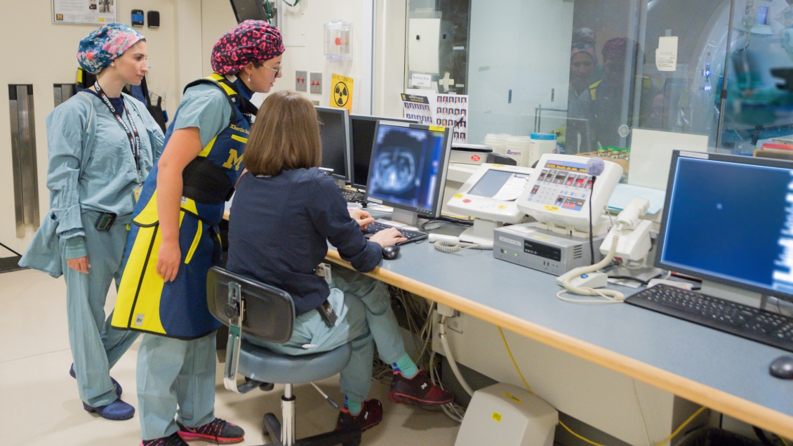 Three female clinicians are gathered around digital screen in Vascular and Interventional radiology control room