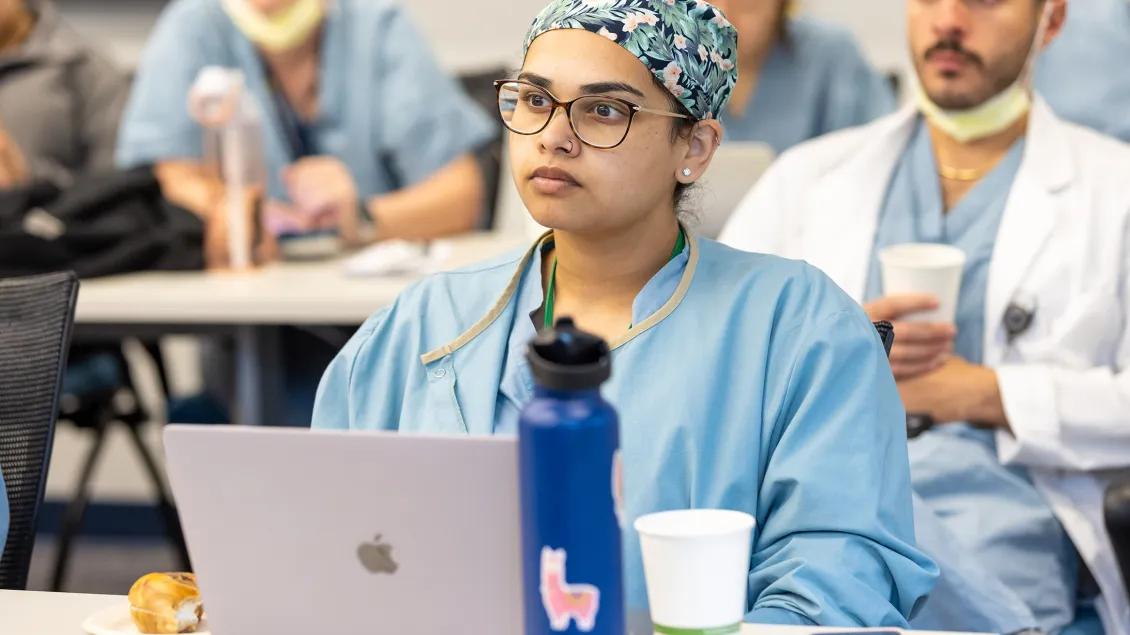 Photo of a woman in scrubs sitting in front of a computer