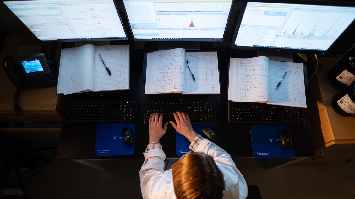 Photo taken from above of a female researcher in front of three monitors in the Metabolomics Core