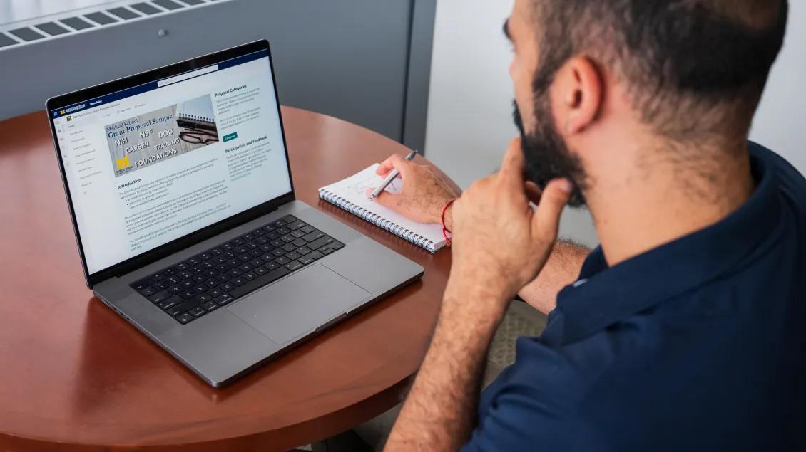 man looking at computer screen of proposal sampler with notebook