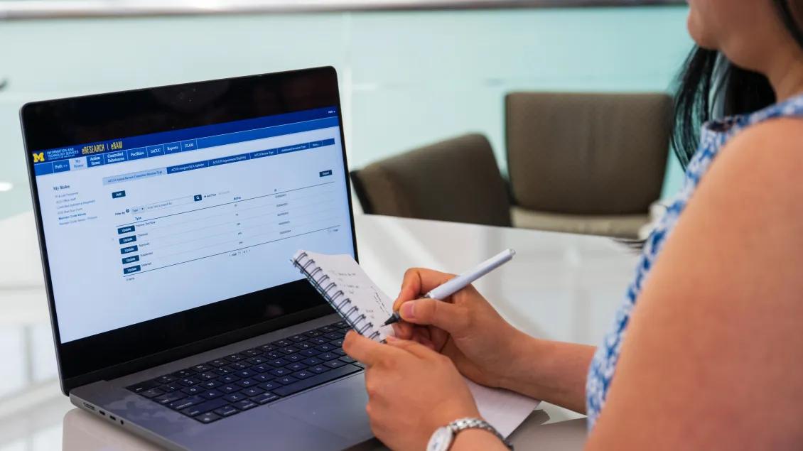 close up of computer screen with eResearch portal displayed; woman taking notes