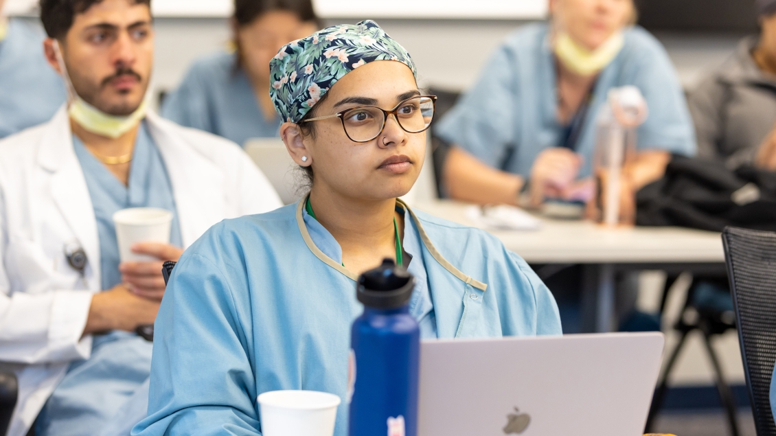 a person in scrubs and glasses sitting at a table with a laptop