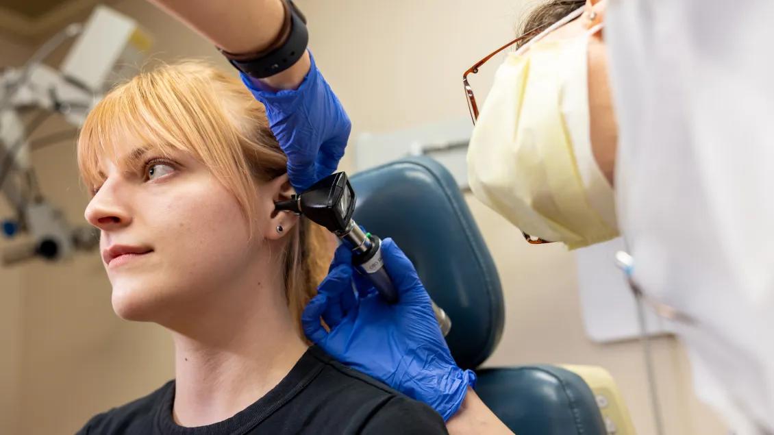 A patient gets her ear examined by a doctor