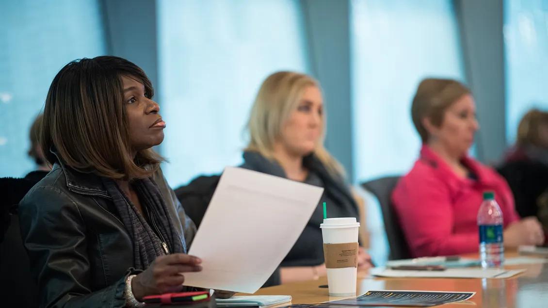 woman focused on presentation in a board meeting, holding a sheet of paper