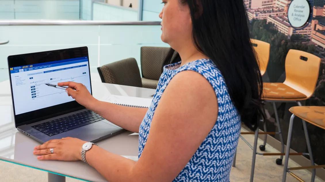 woman pointing at laptop screen with pen; screen is the eResearch portal