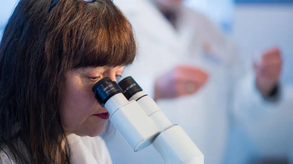 A woman in a lab looking through a microscope