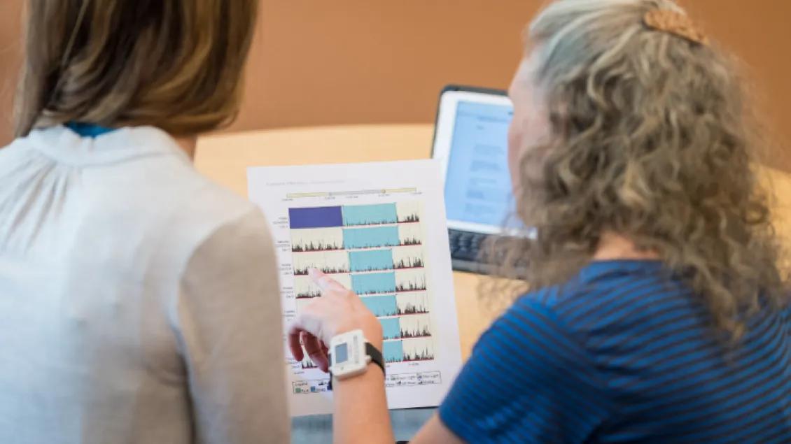 Two women review a printed graph with colorful lines, indicating data analysis.
