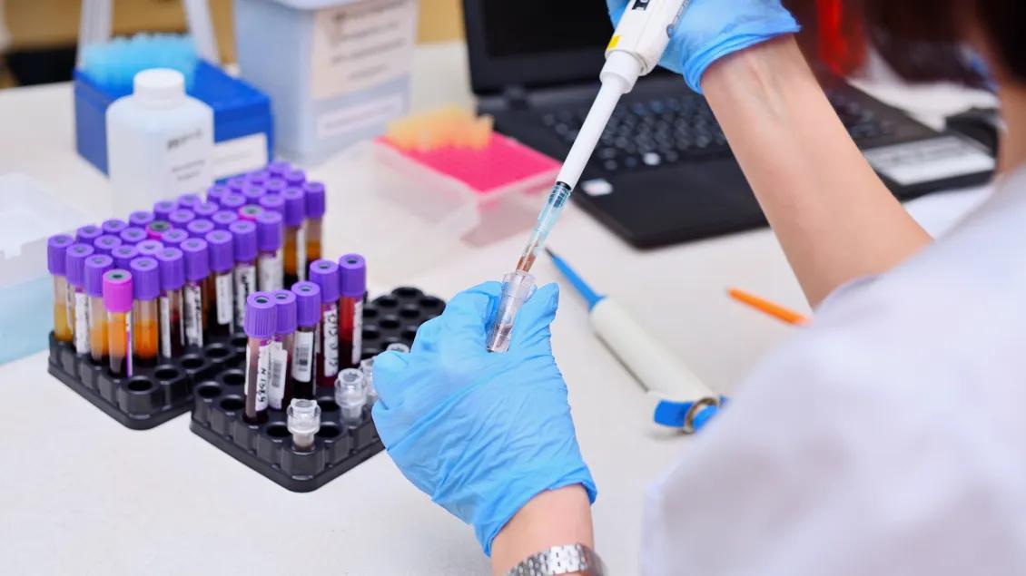 researcher fills test tube while wearing gloves