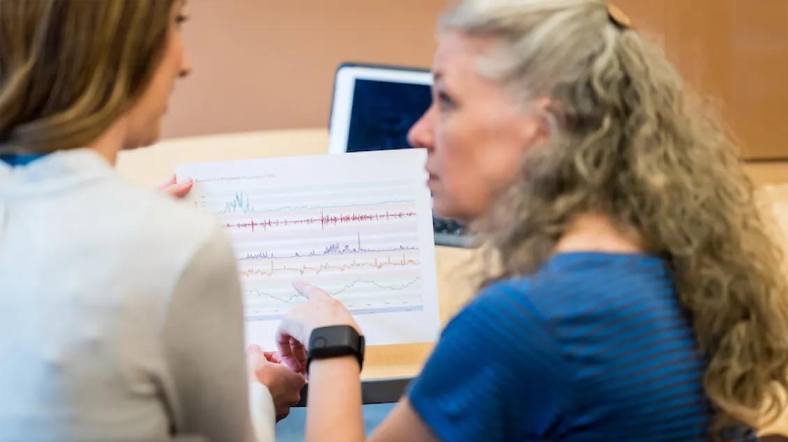 Two women review a printed graph with colorful lines, indicating data analysis.