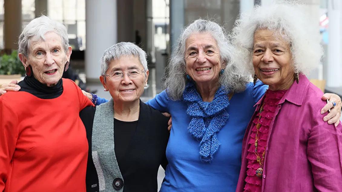 Four older women pose and smile