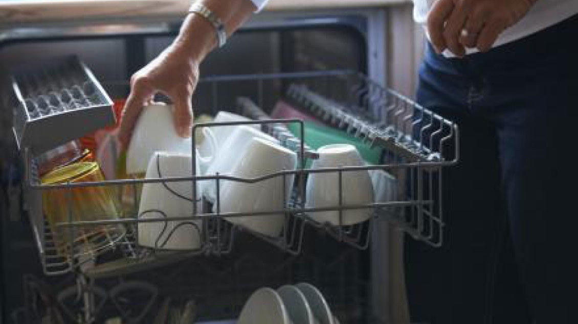 An older woman's hand is shown loading the dishwasher