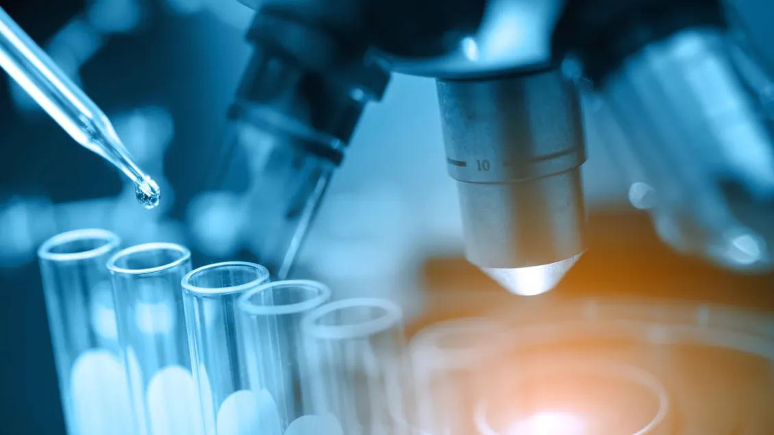 Pipetting into Test Tubes with a Microscope in the background