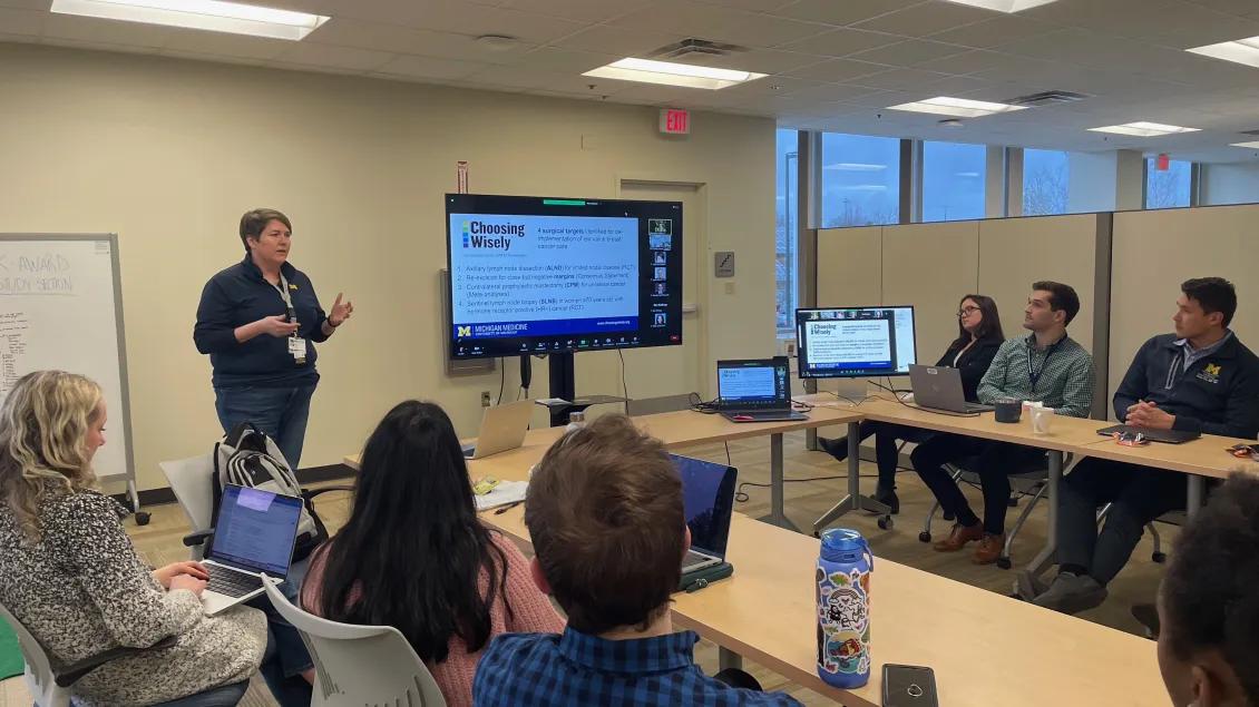 Dr. Dossett giving a presentation to a group of people sitting in a circle of desks