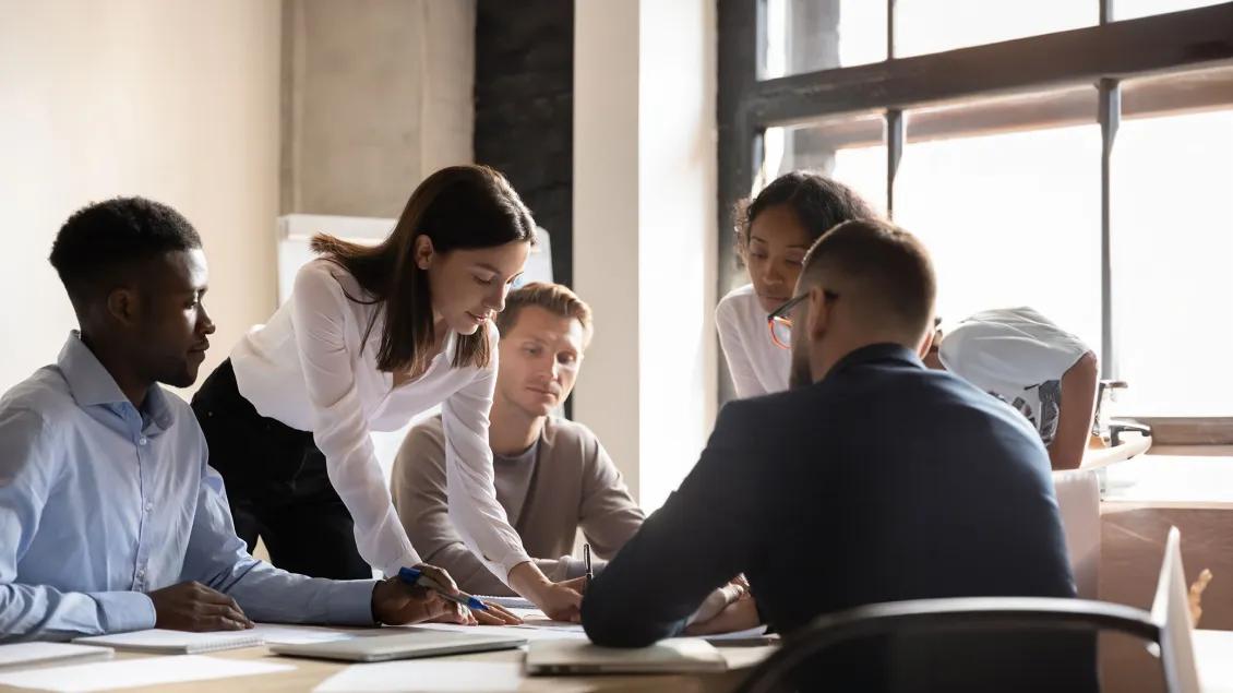 Team of five young researchers discuss a draft proposal at a conference table