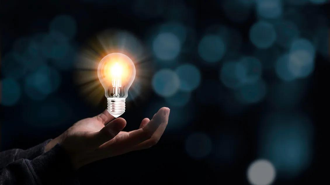 Hand holding a bright light bulb in the dark