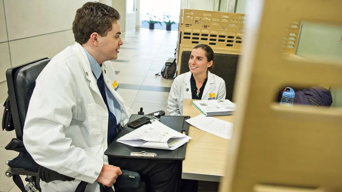 Young female doctor seated and smiling across from young male doctor in a wheelchair