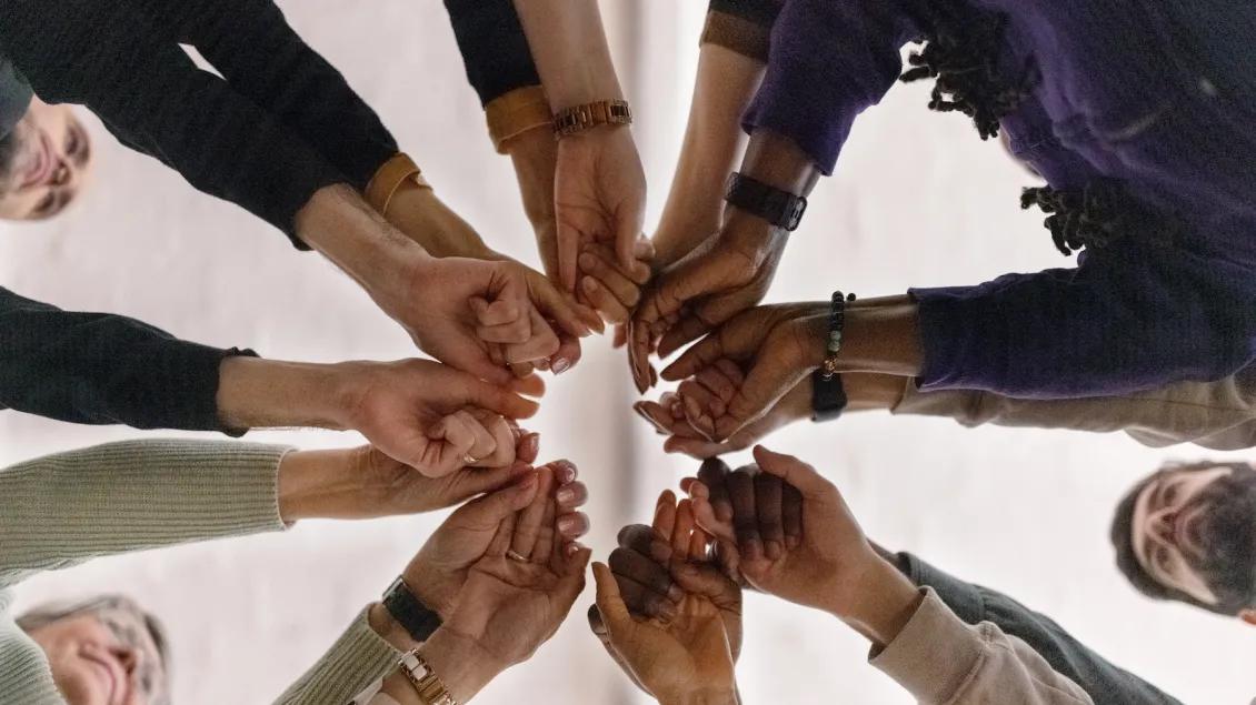 A diverse group of people stand in a circle with hands extended inward