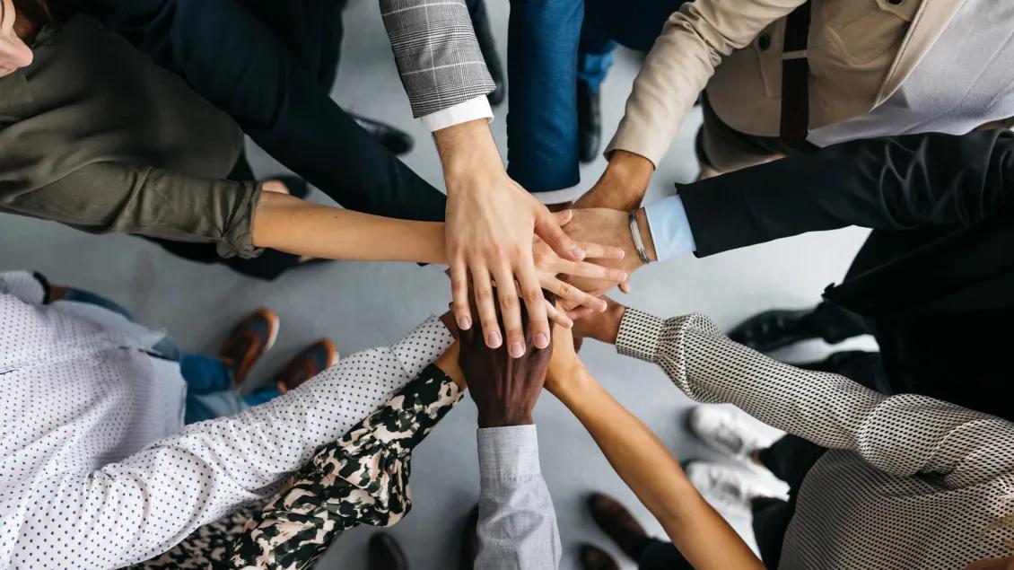 A group of individuals with professional & medical outfits put their hands in the middle of a circle as a team