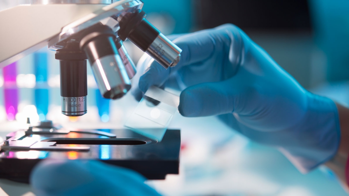 Gloved hand placing a slide under a microscope