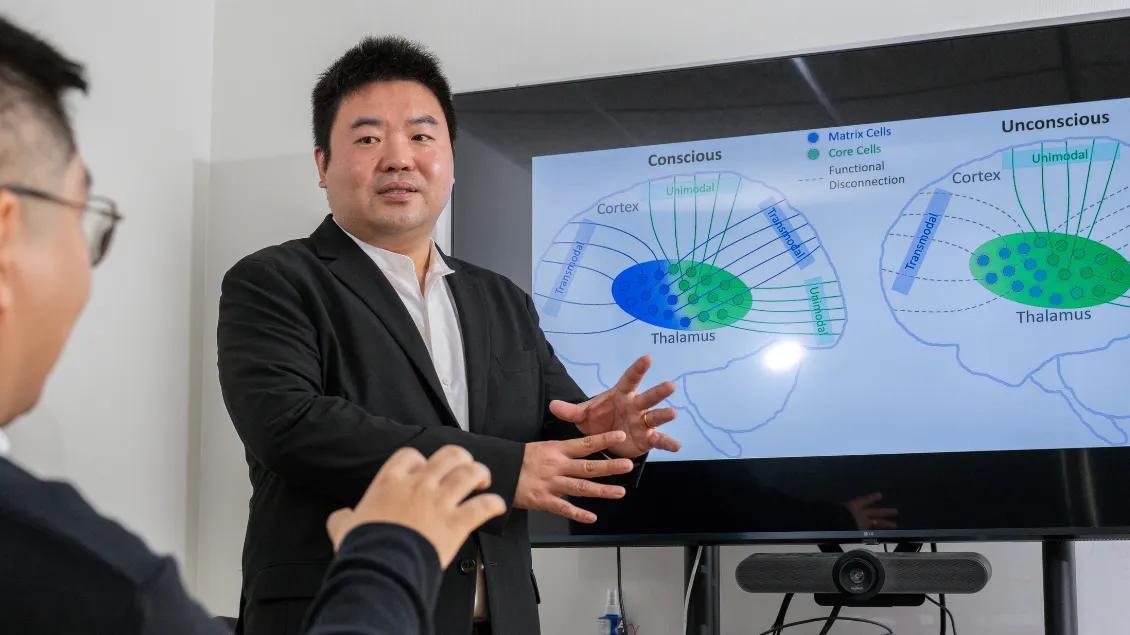two men speaking in front of digital screen with scientific data