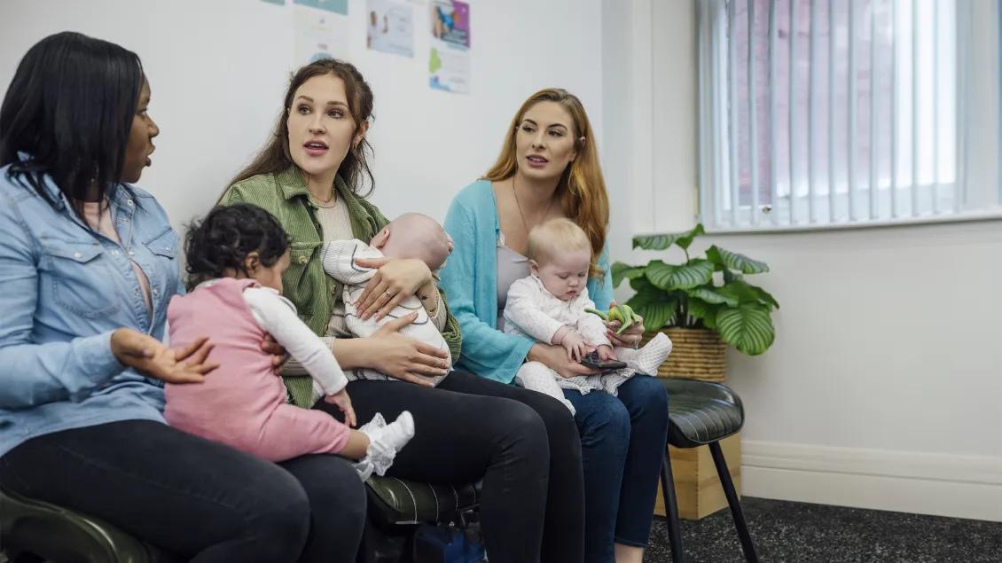three woman with babies speaking in a waiting room