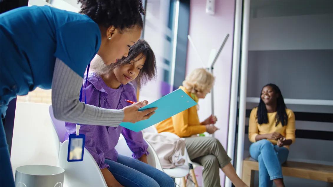 nurse speaking with young girl about a paper form in a waiting room