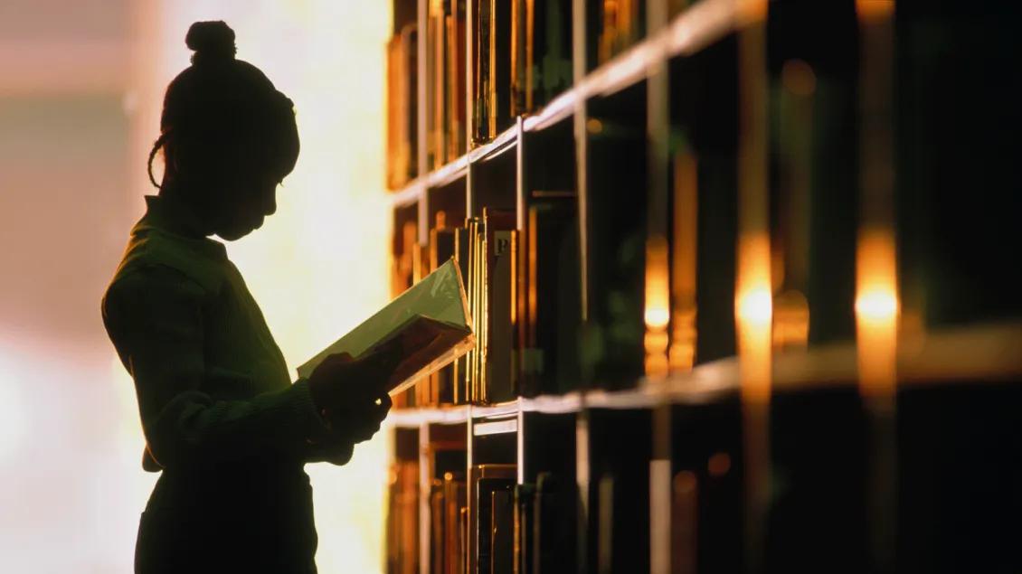 Sihouette of person reading in front of library shelves