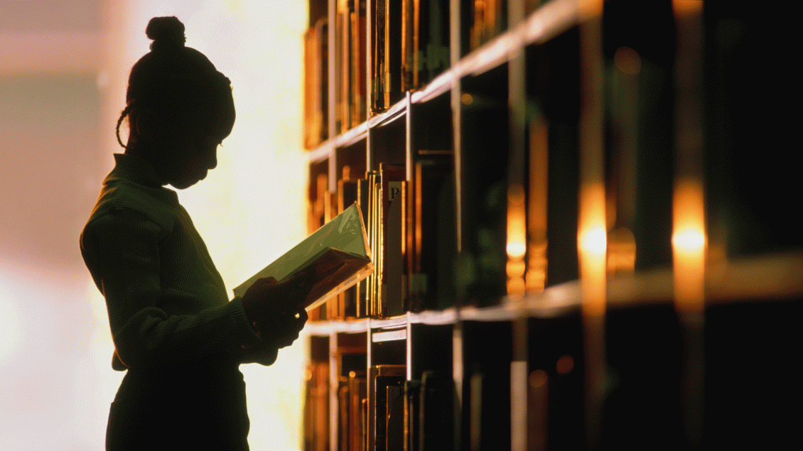 Sihouette of person reading in front of library shelves
