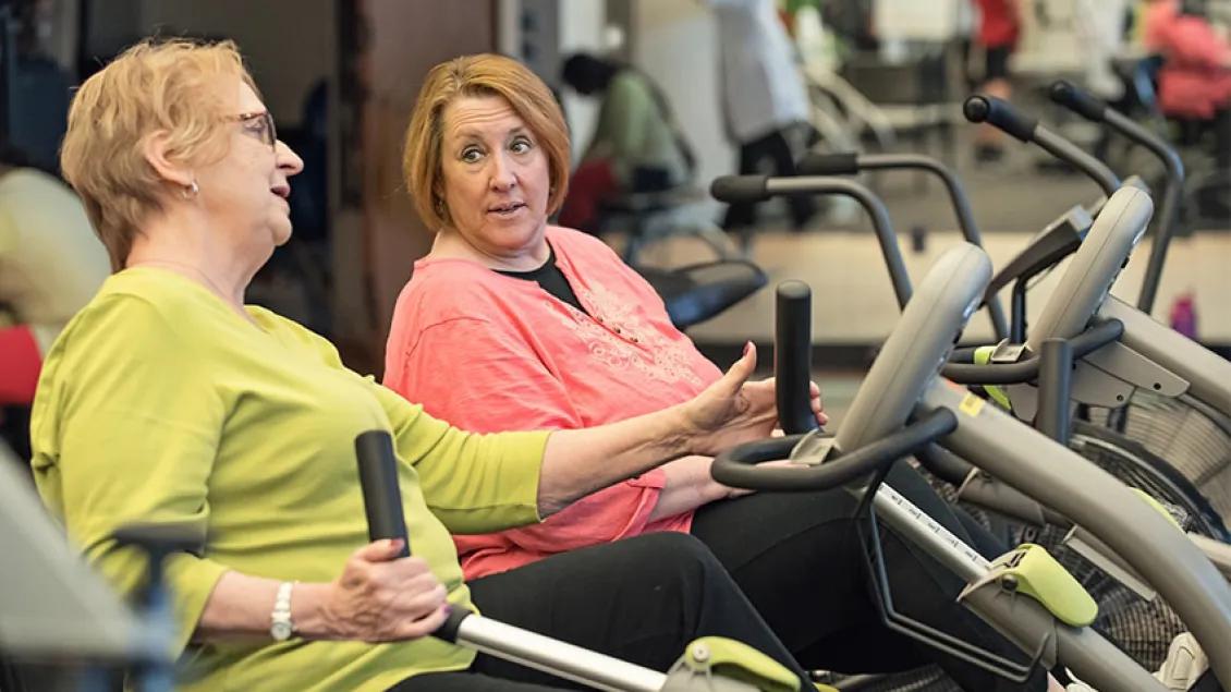 Two women conversing while working on recumbent bikes