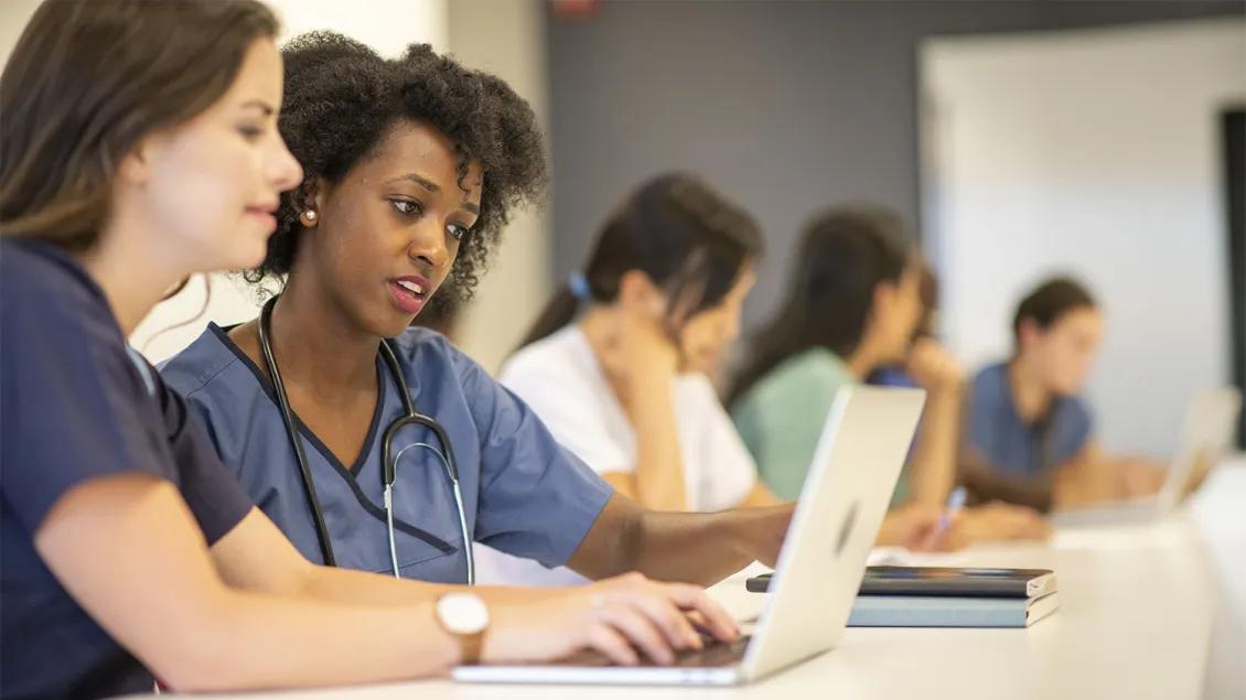 two medical professionals in an educational class with a laptop and notebook