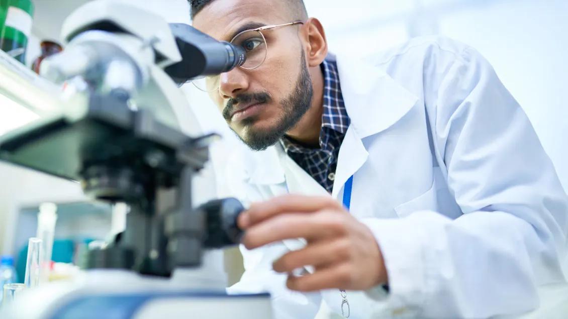 Male scientist looks through microscope