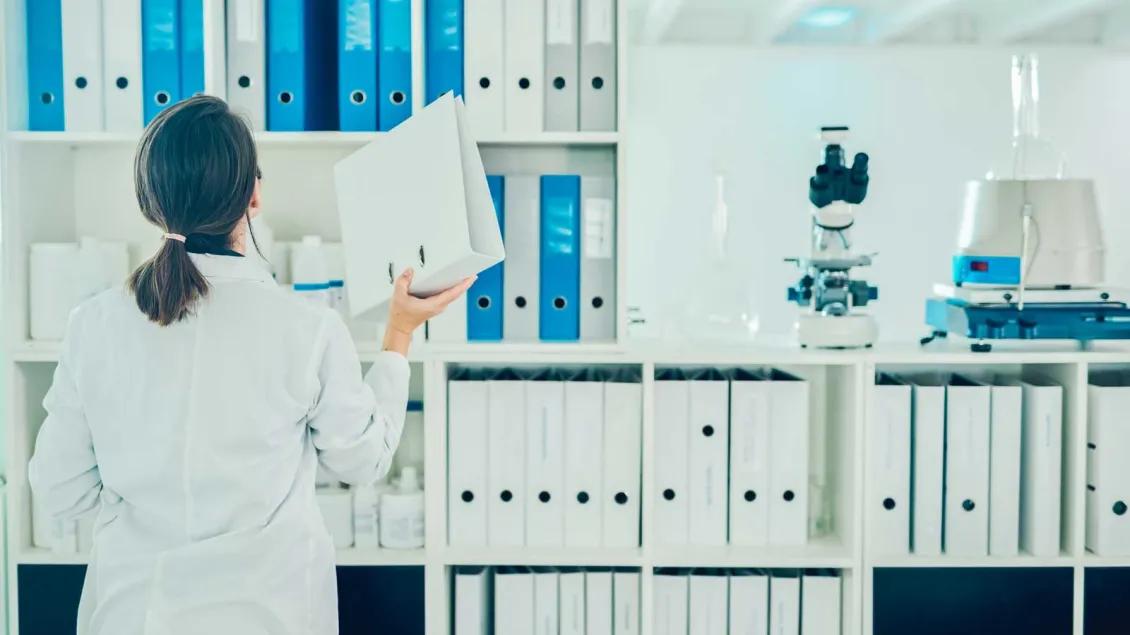 A woman with a ponytail reshelves a binder into a wall full of binders on shelves