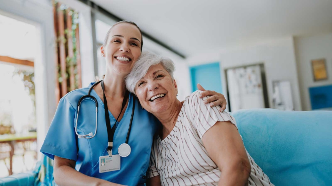 Nurse hugging white-haired senior on a couch