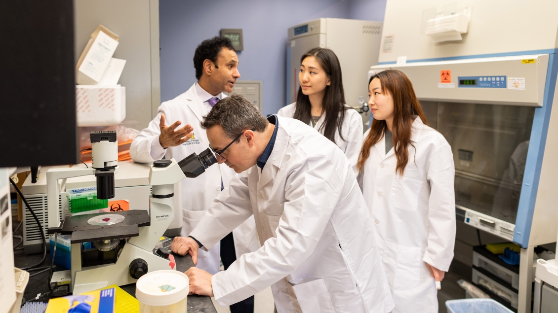 Four researchers gathered around a microscope in a lab
