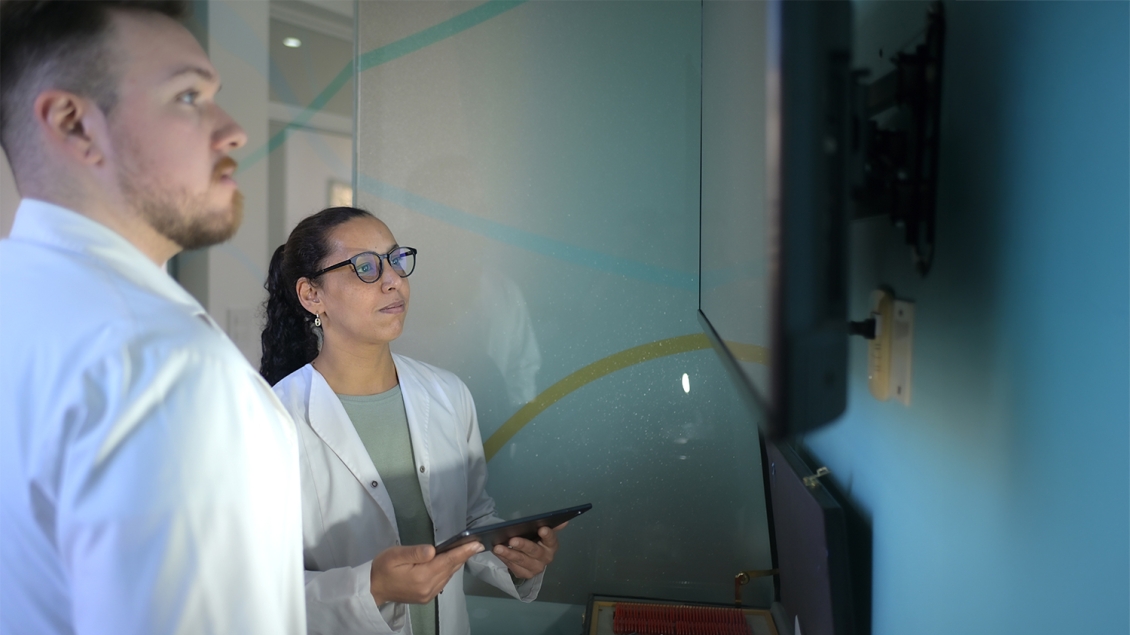 man and woman in lab coats using tablet to project on a large display monitor