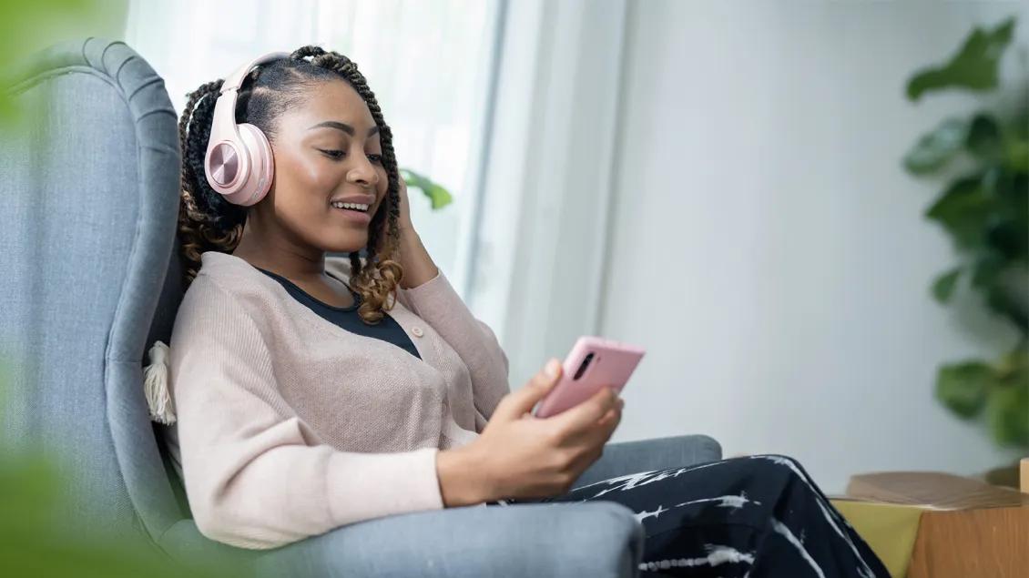 woman sitting and smiling while listening to a podcast on headphones