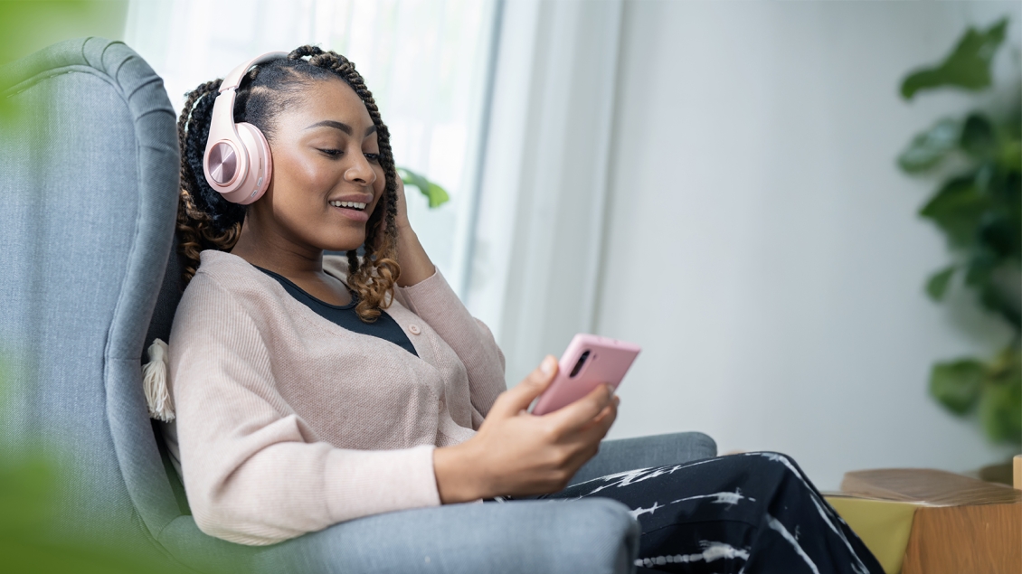 woman sitting and smiling while listening to a podcast on headphones